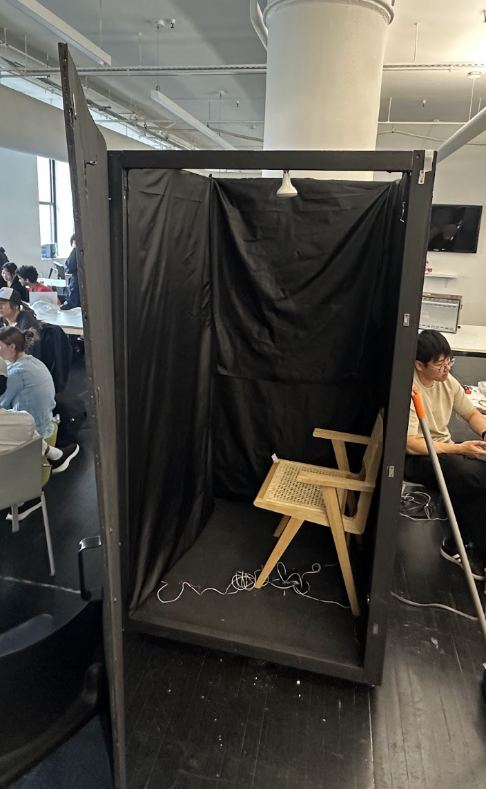 The finished booth: a black box on wheels with its door open, black fabric inside and a wooden chair
