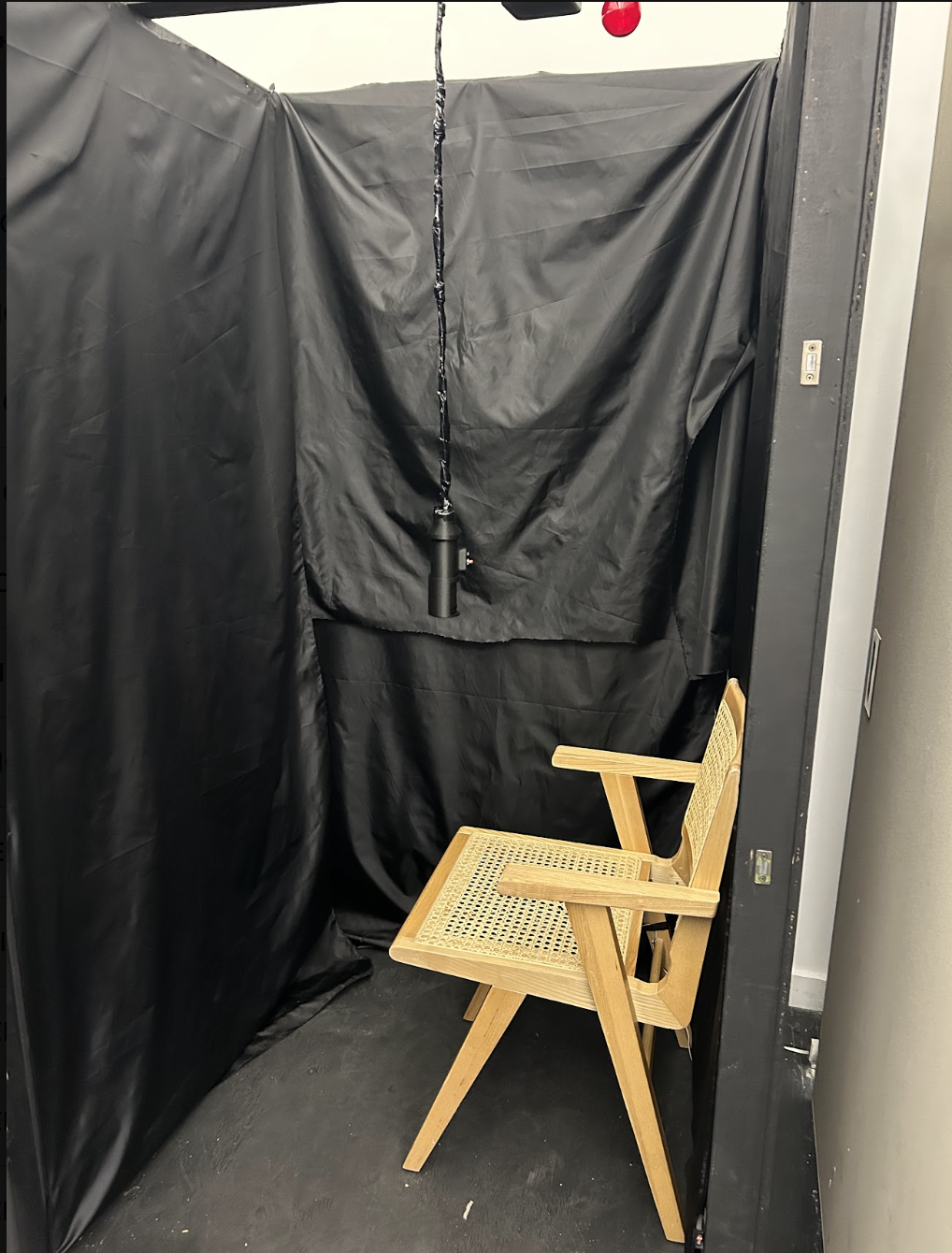 Inside the finished booth: black fabric walls, a wooden cane chair and a fixture hanging from the ceiling