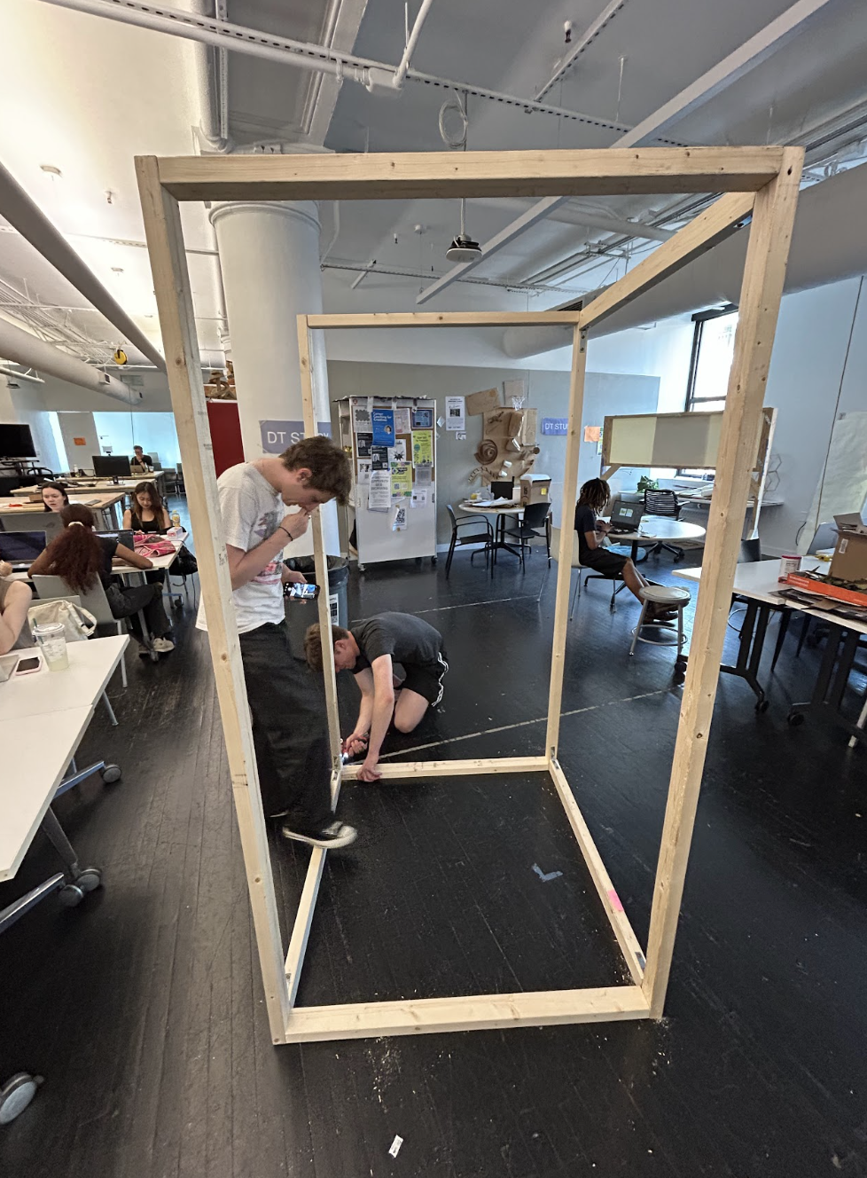 Two team members assembling the 2x4 wooden frame of the booth in the studio